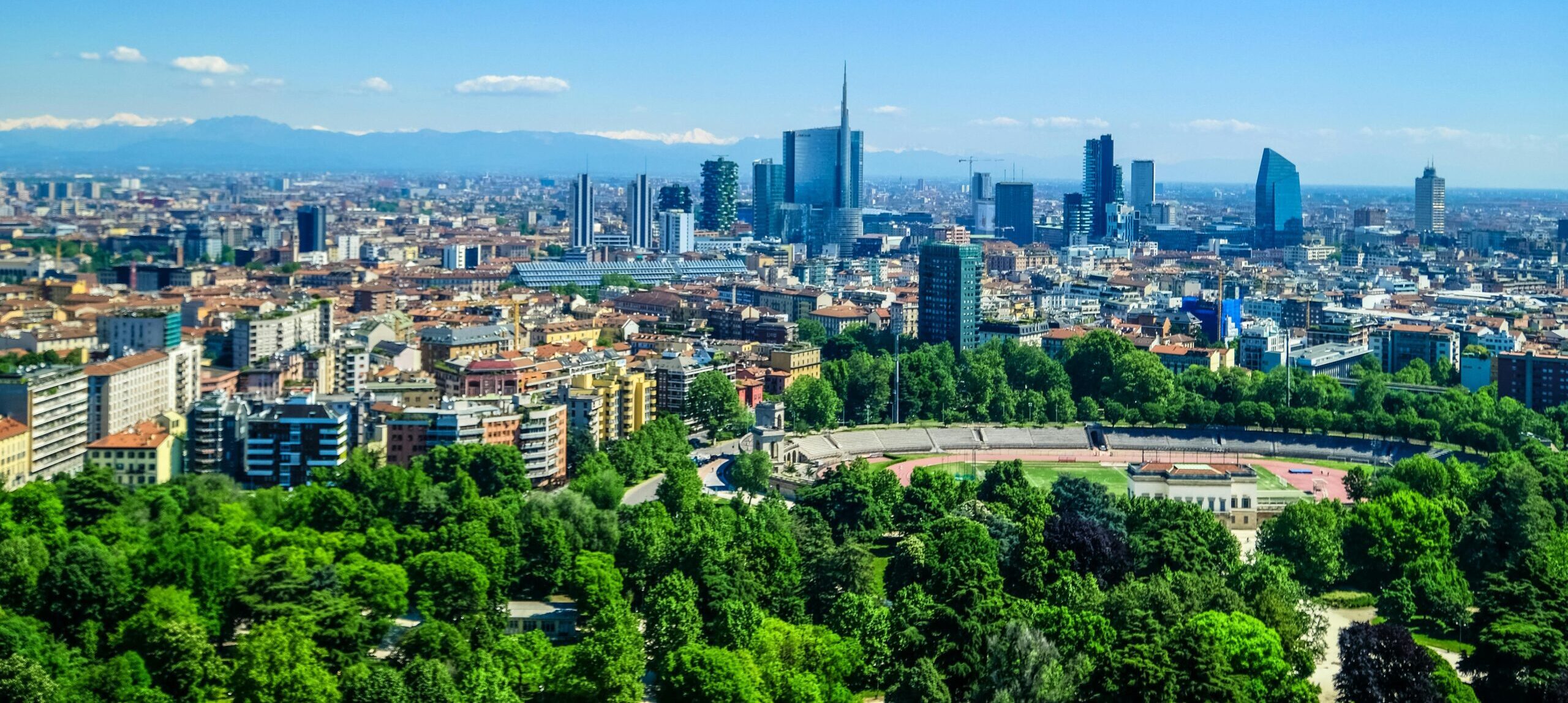 Panoramic view of Milan's skyline featuring modern skyscrapers and lush greenery under a clear blue sky.