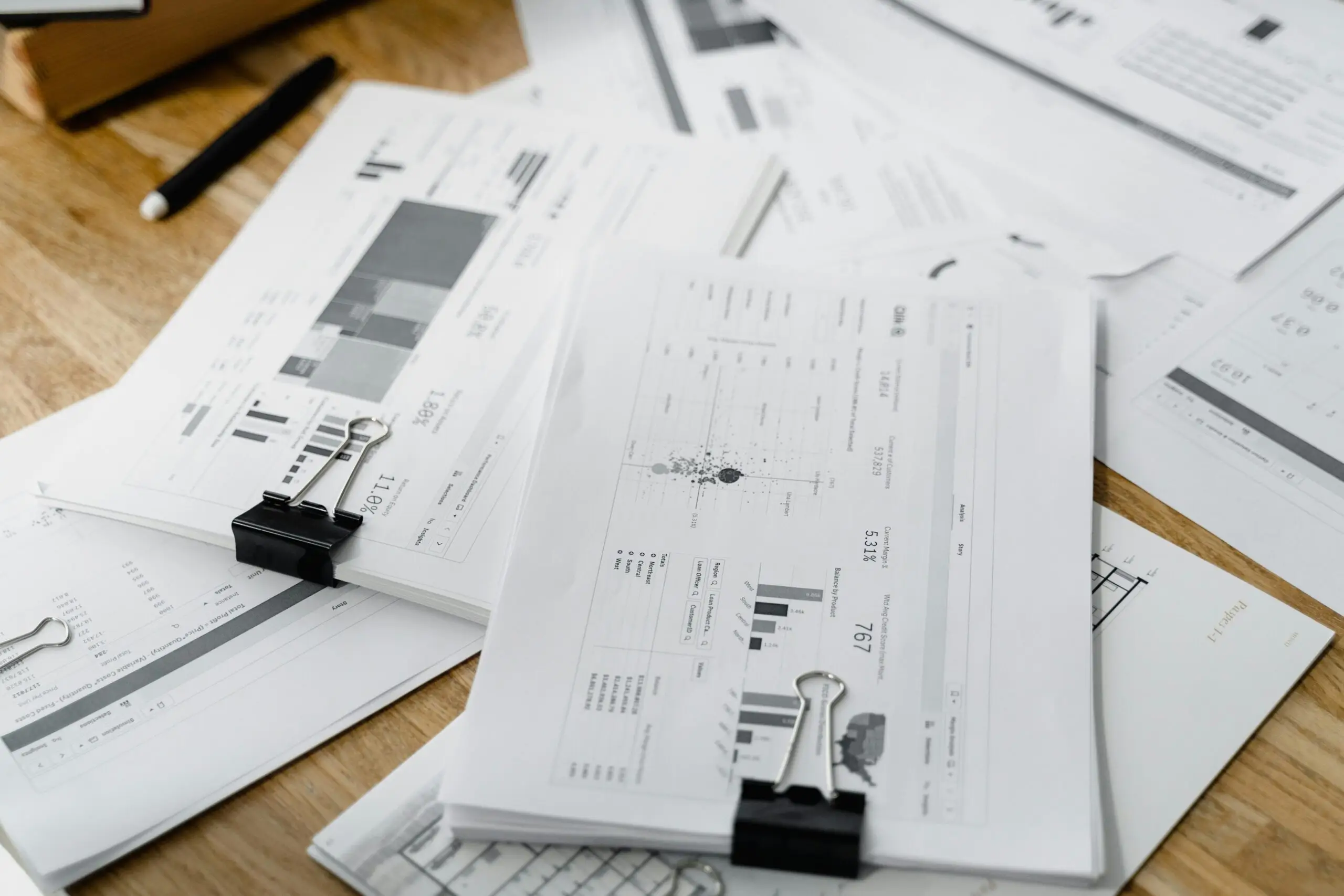 A stack of financial reports and graphs with clips on a wooden desk, highlighting business planning.